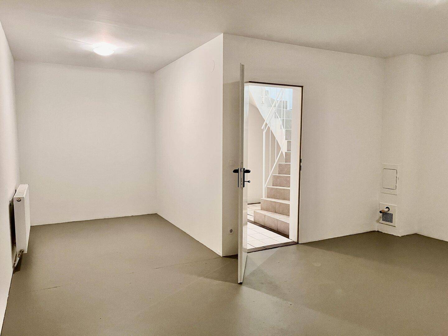 Kellerraum mit grauem Boden und Tür, die zu einer Treppe ins obere Stockwerk führt.