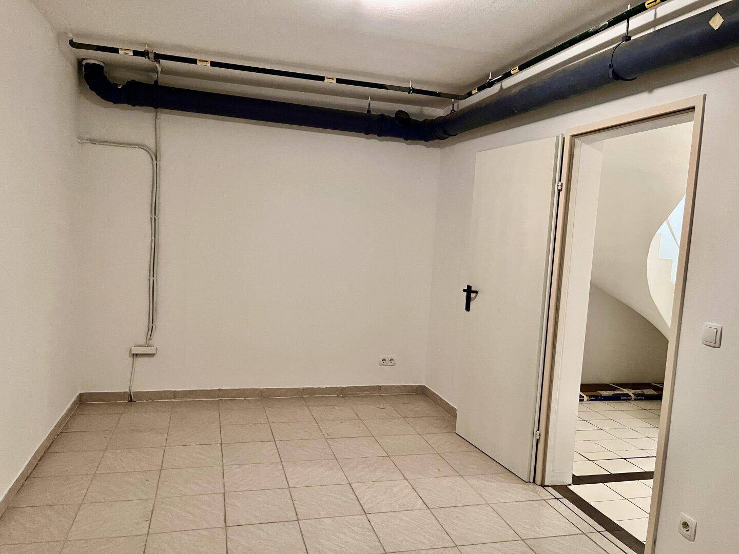 Kellerraum mit Fliesenboden und freiliegenden Rohren, der als Abstell- oder Technikraum dient.