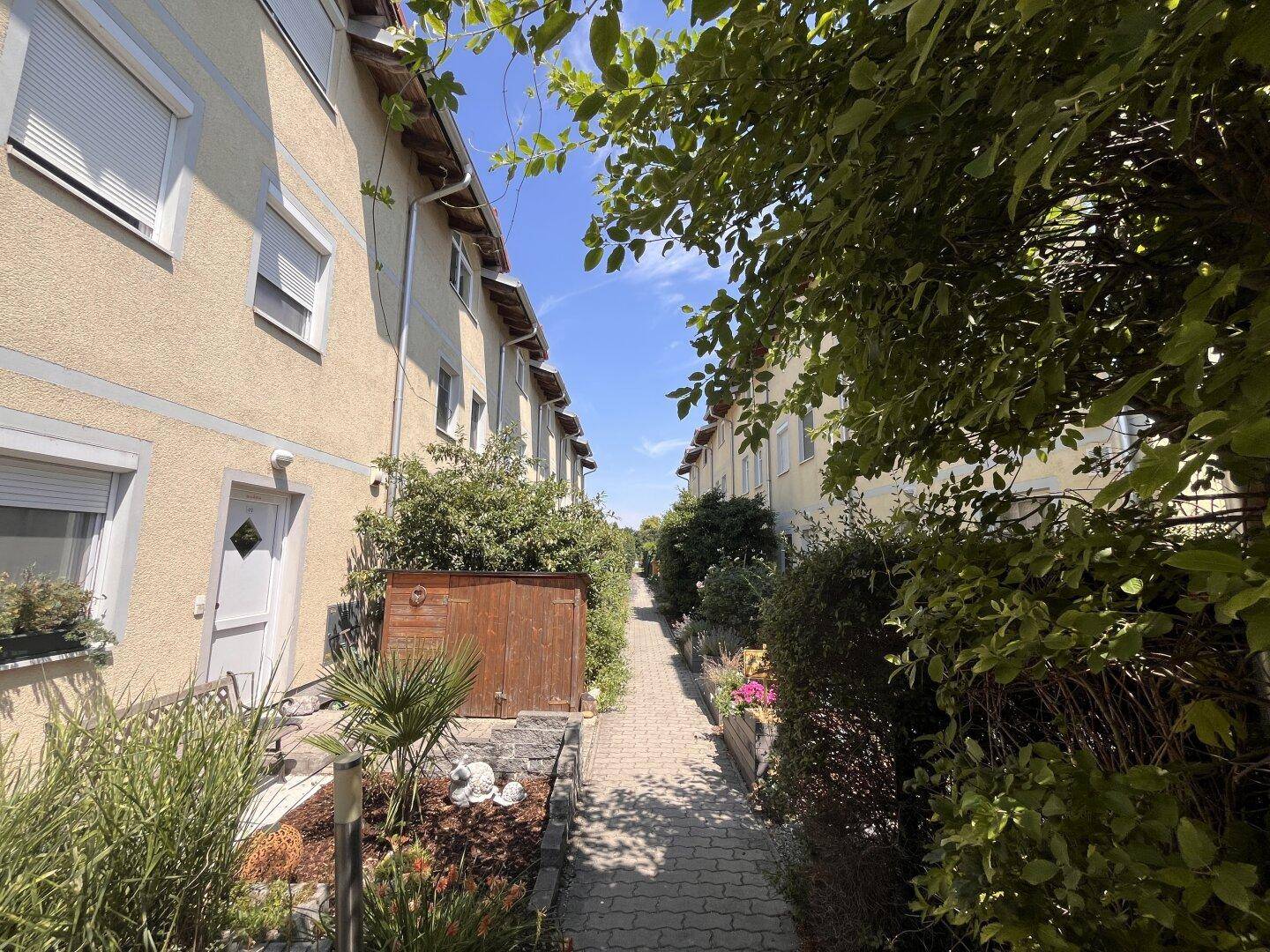 Idyllischer Fußweg zwischen Reihenhäusern, gesäumt von gepflegten Gärten und Sträuchern.