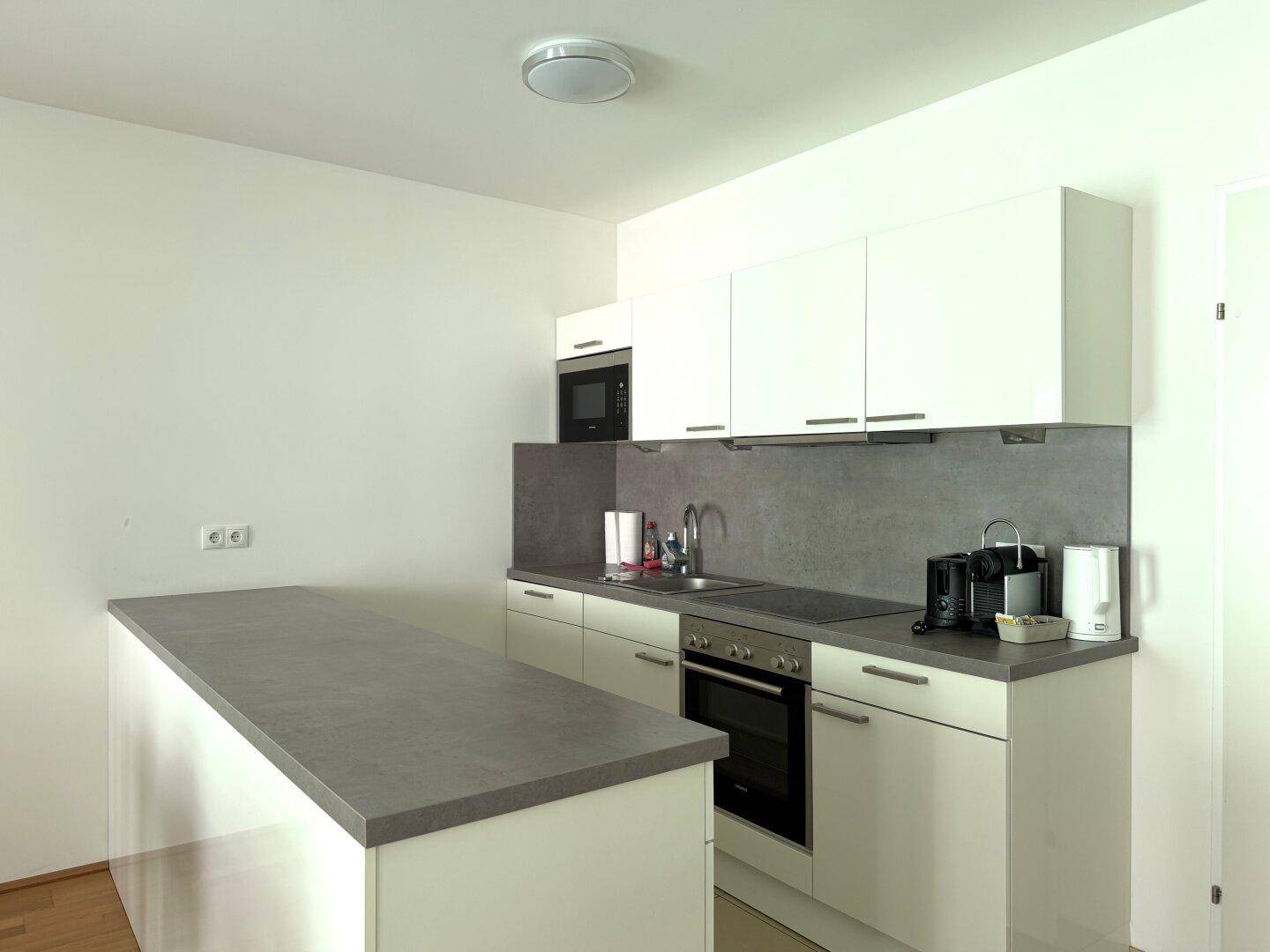 Moderne Einbauküche mit weißen Hochglanzfronten, grauer Arbeitsplatte und integrierten Geräten.