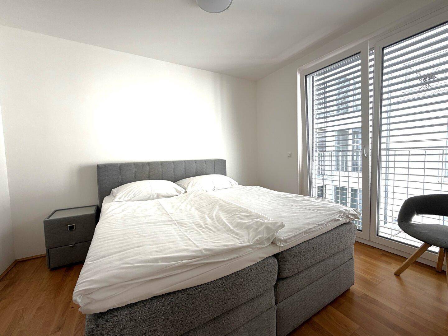 Gemütliches Schlafzimmer mit Holzboden und viel Tageslicht durch das große Fenster.