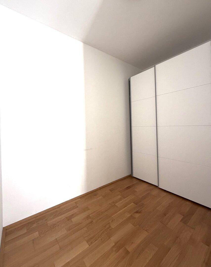 Leeres Zimmer mit Holzboden und einem praktischen weißen Schiebetürenschrank.