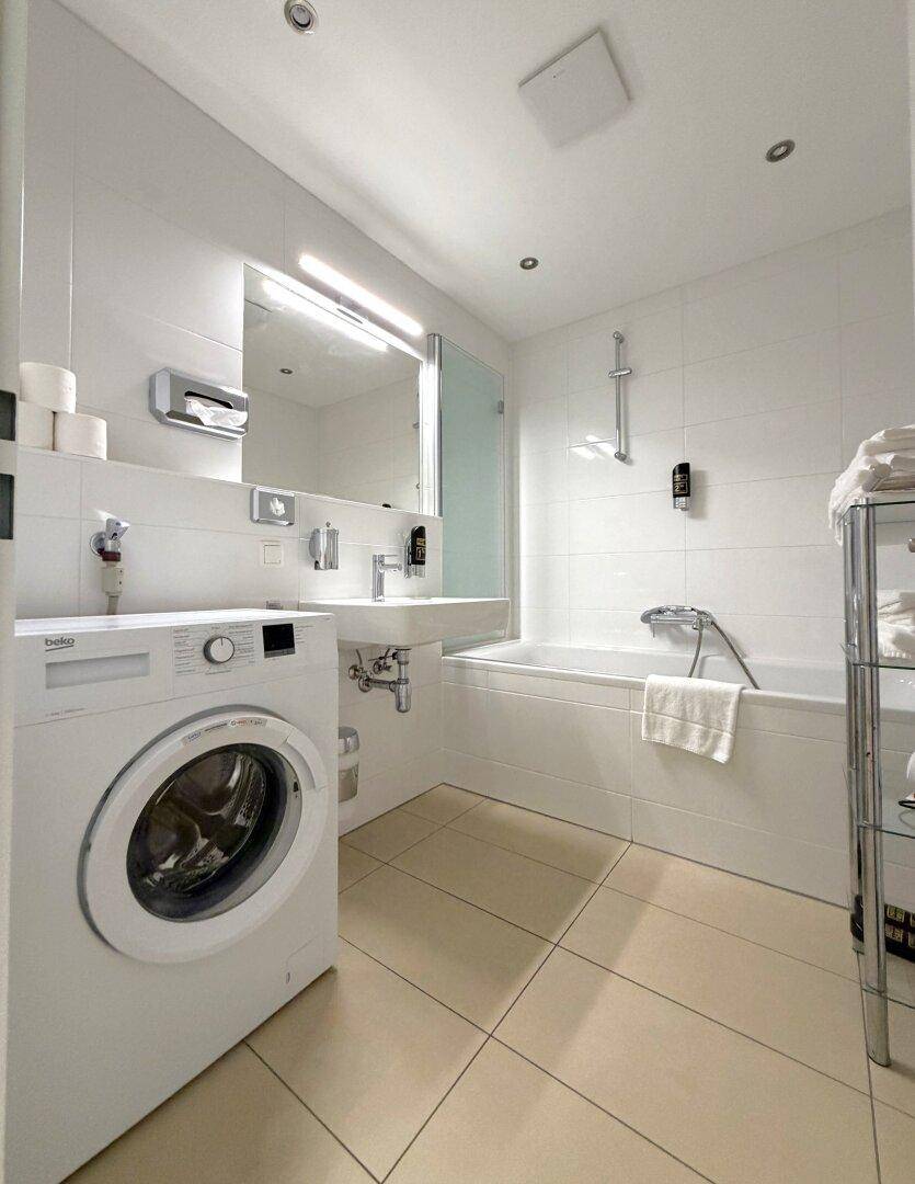 Helles Badezimmer mit Badewanne, Waschbecken und integrierter Waschmaschine für Komfort.