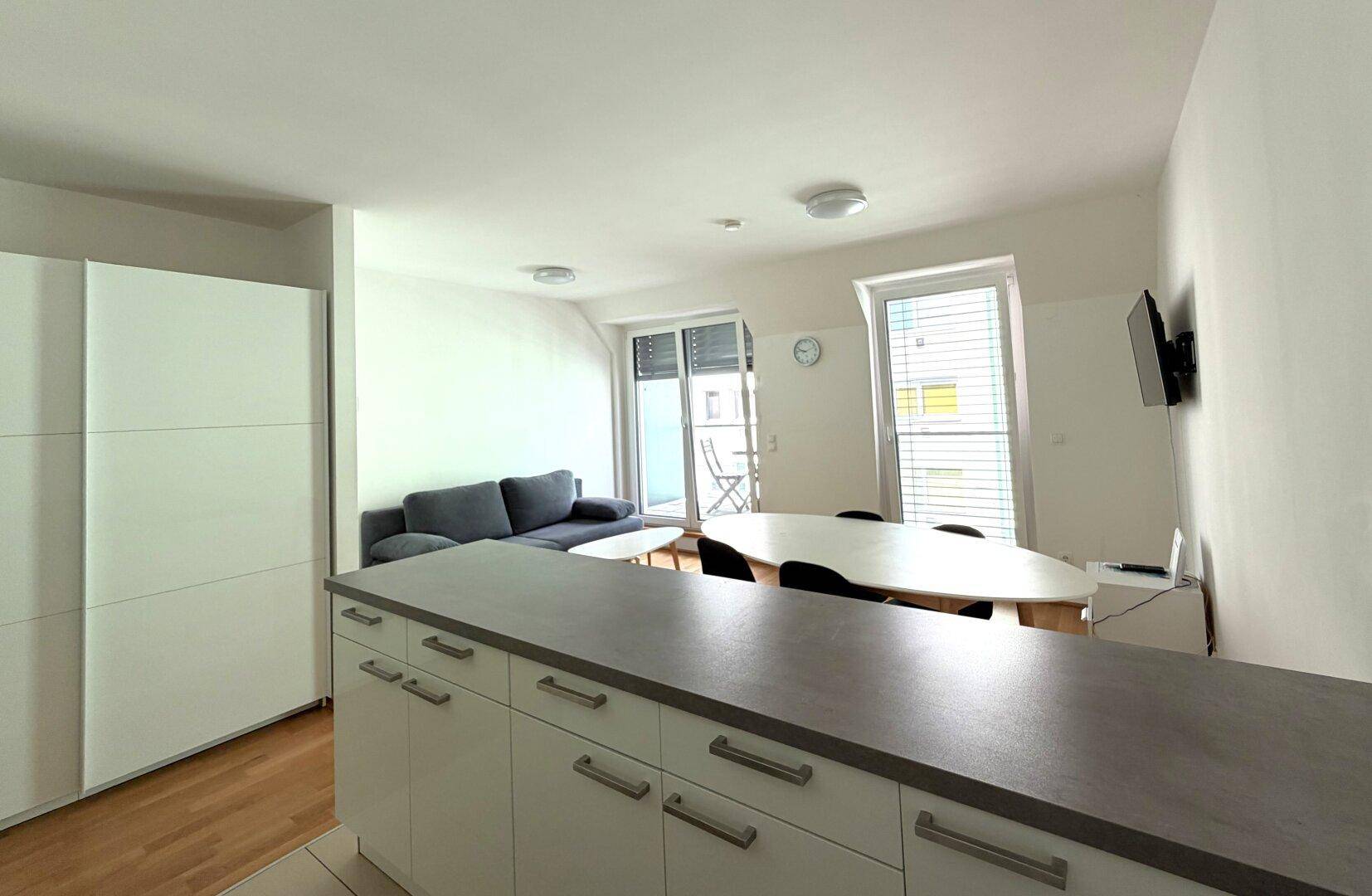 Blick von der Küche in den Wohnbereich mit Balkonzugang und einem großen weißen Einbauschrank.