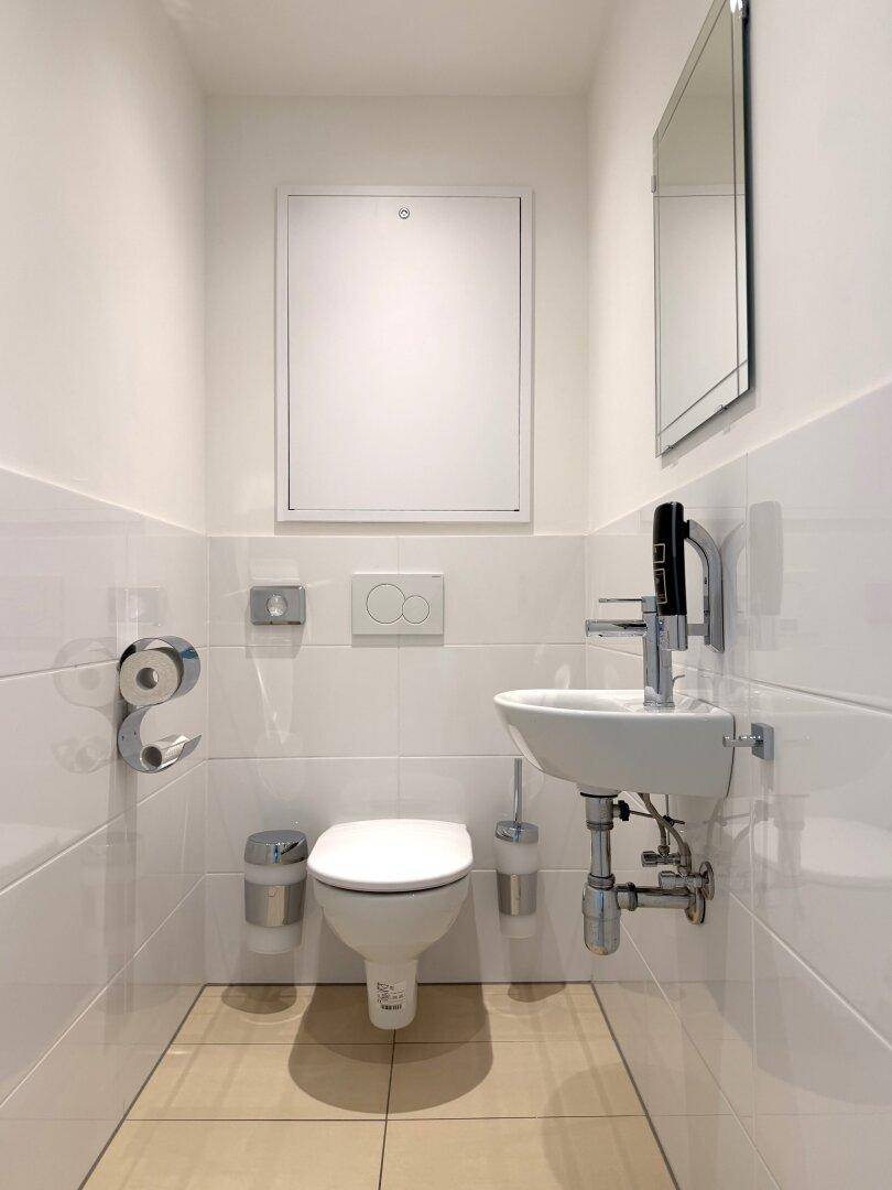 Separates Gäste-WC mit wandhängender Toilette, kleinem Waschbecken und Spiegel.