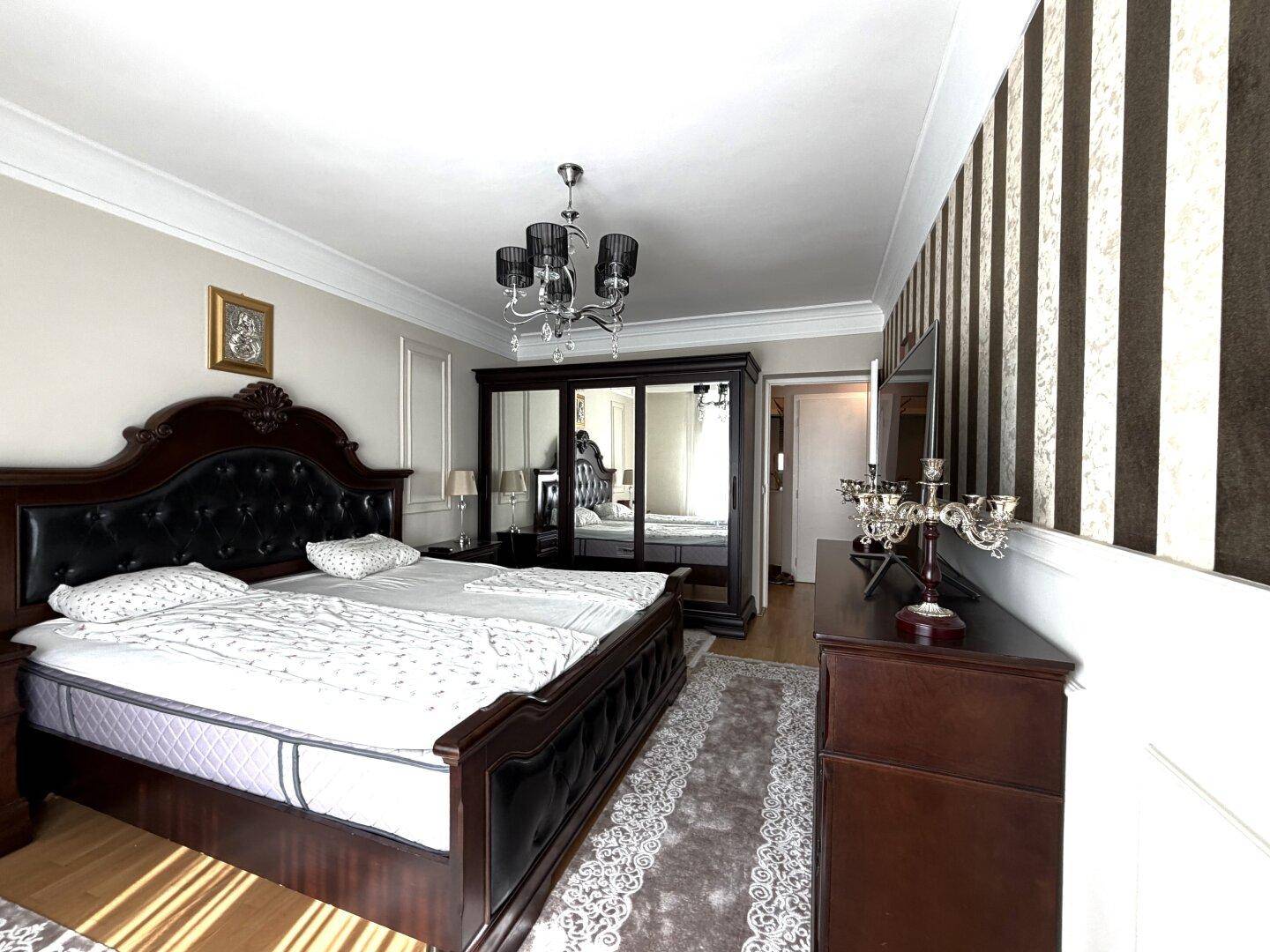 Elegantes Schlafzimmer mit großem dunklen Holzbett, Spiegelschrank und stilvoller braun-beiger Tapete.