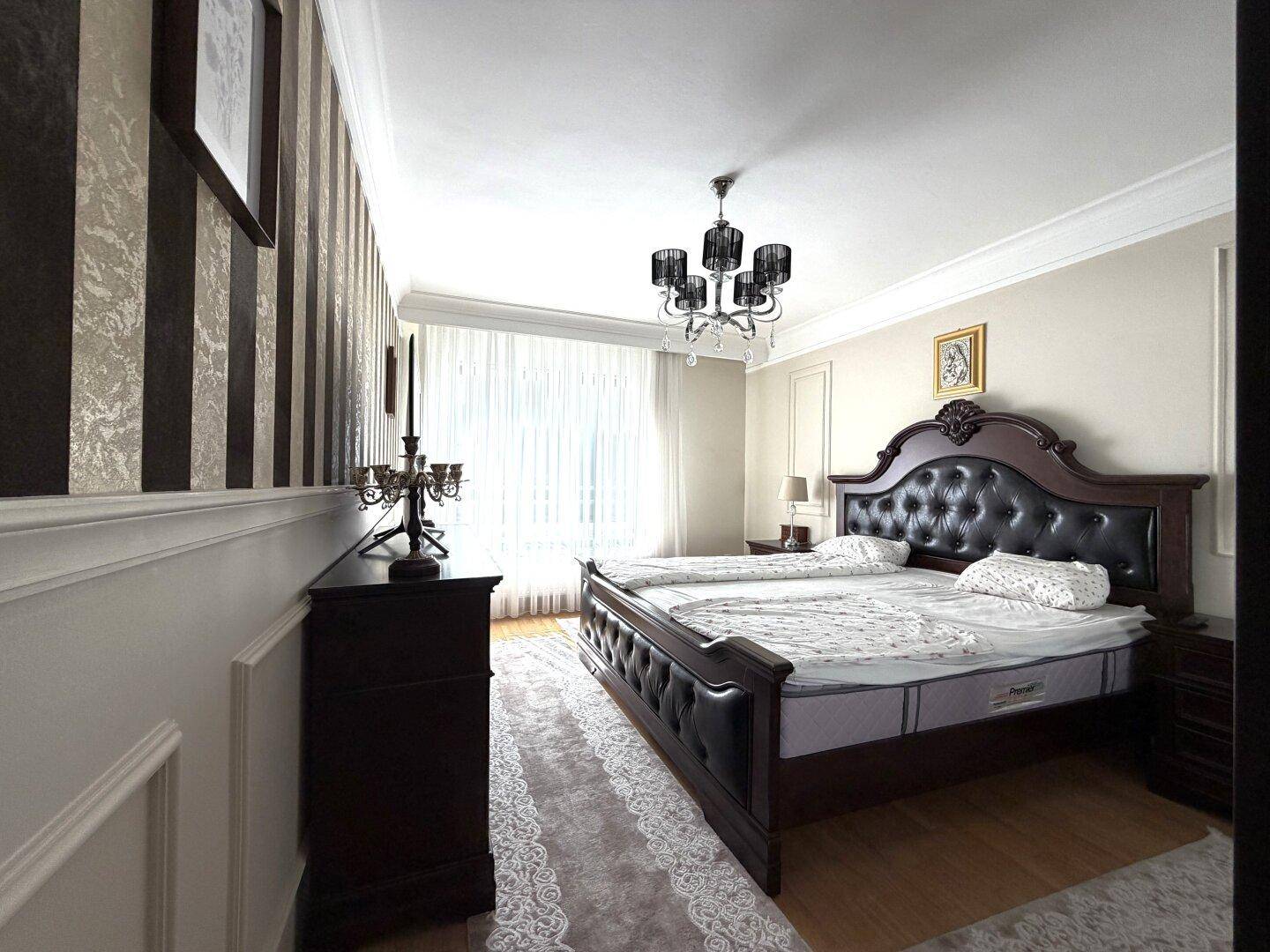 Helles Schlafzimmer mit großem Holzbett, eleganten Möbeln und viel Tageslicht durch das Fenster.