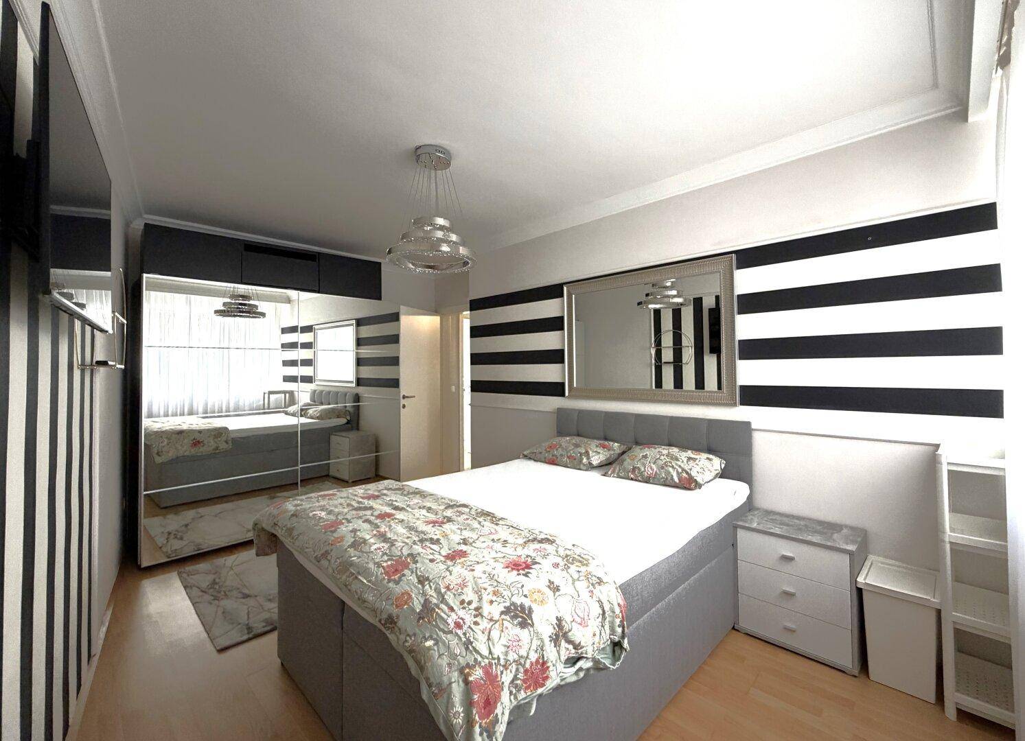 Modernes Schlafzimmer mit großem Bett, Spiegelschränken und auffälliger schwarz-weiß gestreifter Tapete.