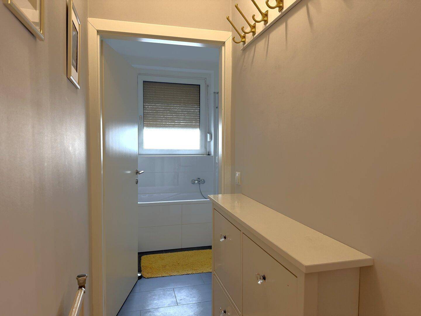 Flur mit Zugang zum Badezimmer, das eine Badewanne und ein Fenster zeigt.