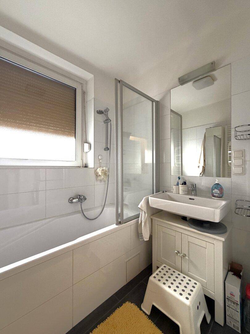 Helles Badezimmer mit Badewanne, Duschabtrennung, Fenster und einem einzelnen Waschbecken.
