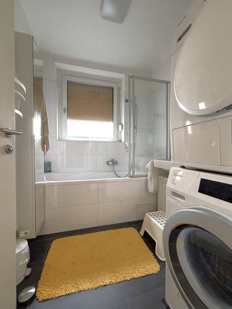 Funktionales Badezimmer mit Badewanne, Fenster und praktischer Waschmaschine und Trockner.