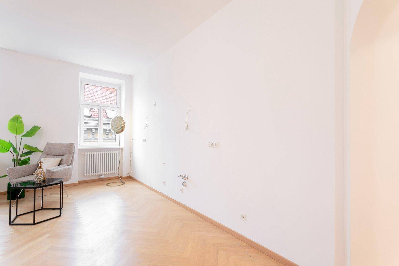 Heller Raum mit Fischgrätparkett, einem Sessel und einem Fenster mit Blick nach draußen.