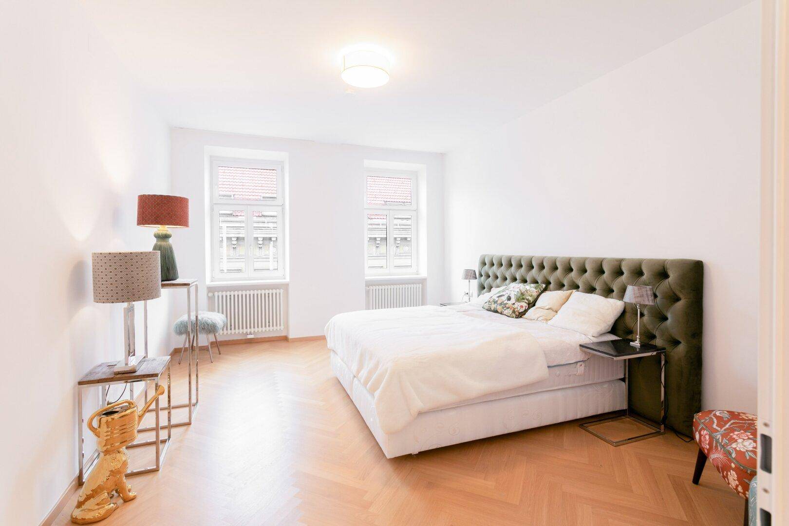 Großes Schlafzimmer mit Doppelbett, gepolstertem Kopfteil und hellem Fischgrätparkett.