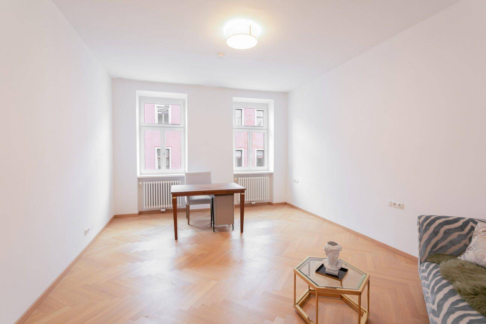 Helles Arbeitszimmer mit Schreibtisch, Fischgrätparkett und zwei Fenstern.