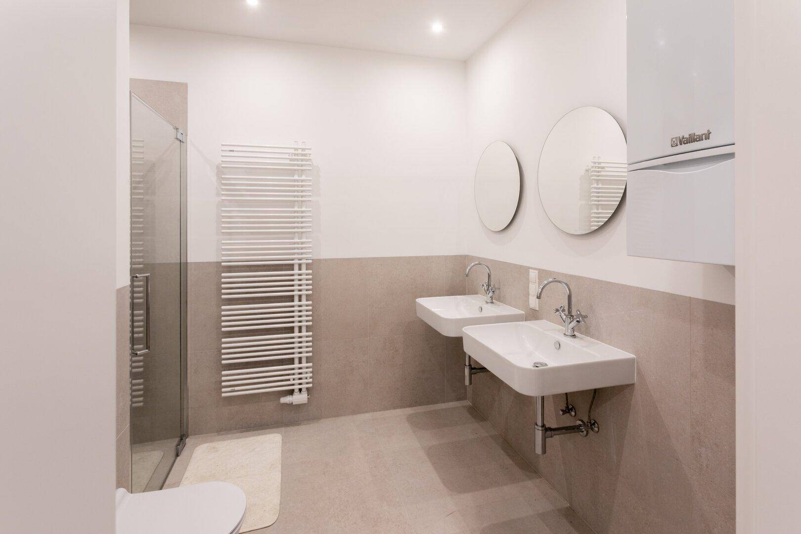Modernes Badezimmer mit zwei Waschbecken, Duschkabine und beheiztem Handtuchhalter.