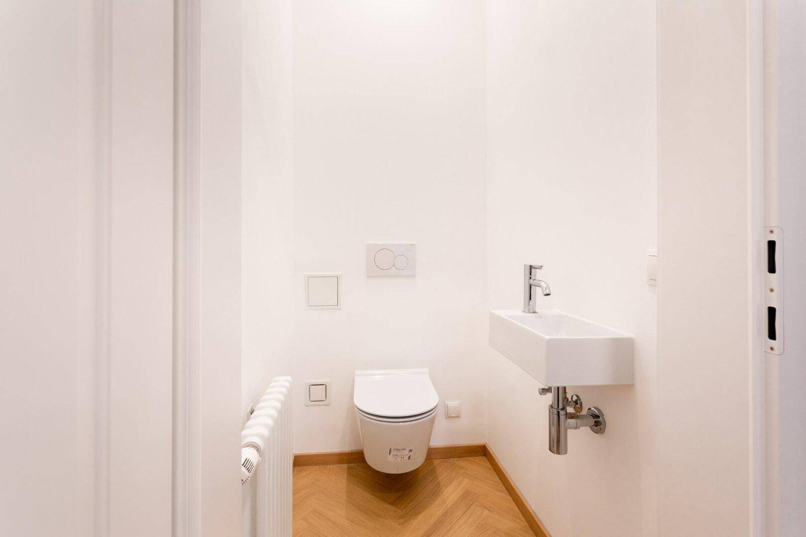 Separates Gäste-WC mit Wand-WC, kleinem Waschbecken und Heizkörper.