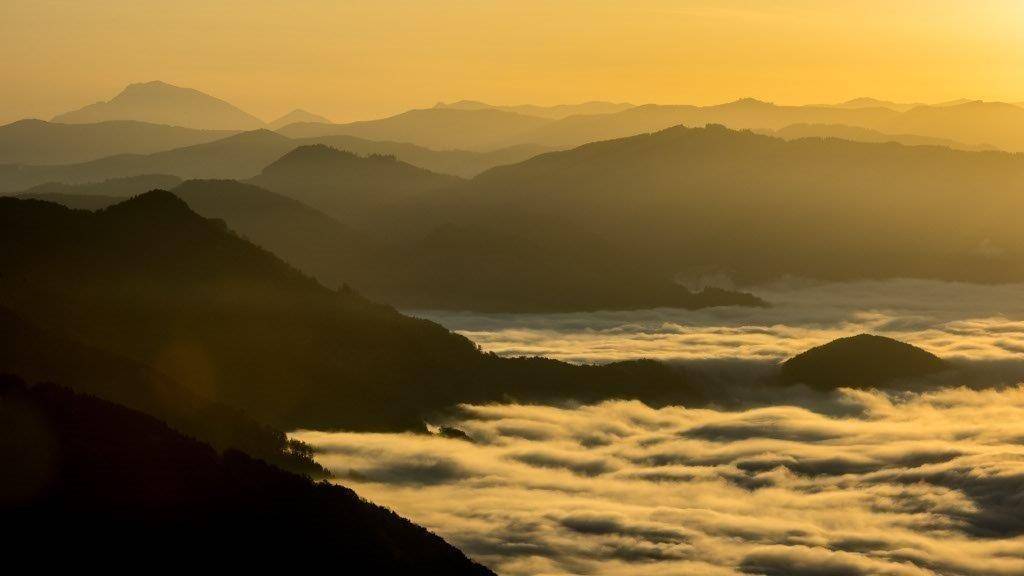 Goldener Sonnenuntergang über einer Berglandschaft mit dichten Nebelschwaden.