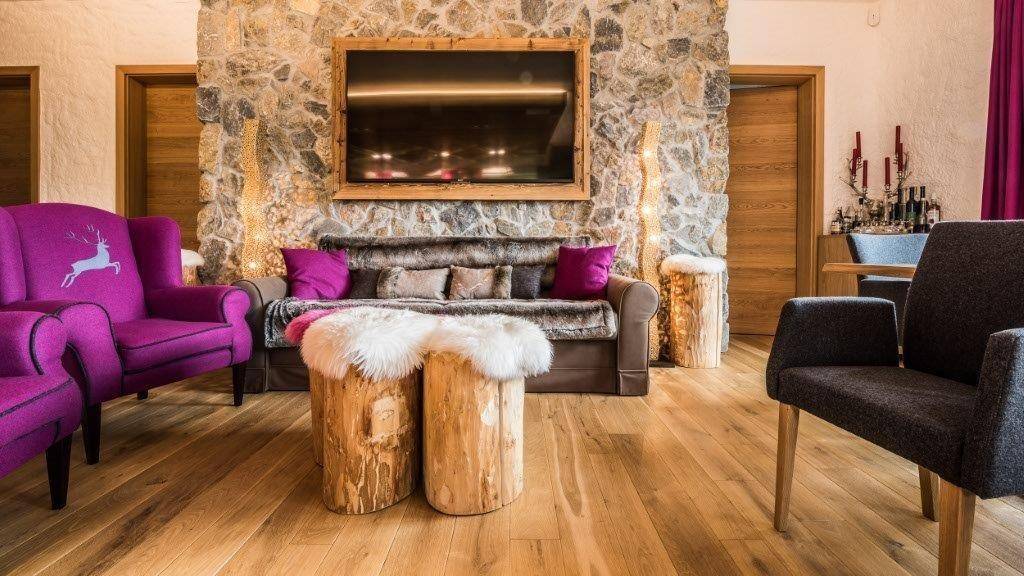 Gemütliches Wohnzimmer im alpinen Stil mit Steinwand, Holzboden und farbigen Akzenten.