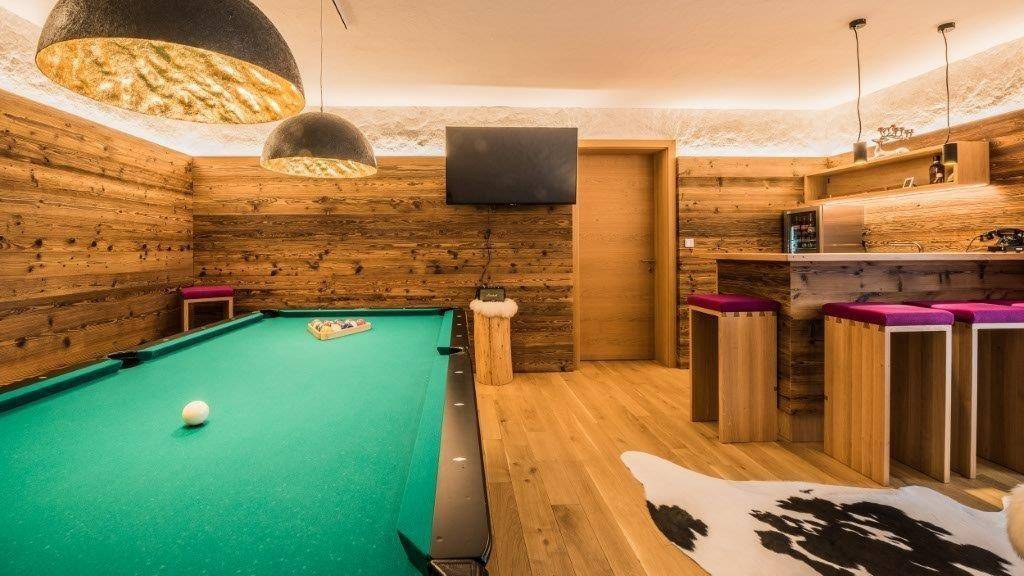Spielzimmer mit Billardtisch, Holzvertäfelung und einer kleinen Bar.
