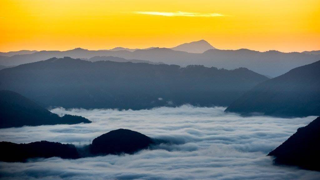 Dramatischer Sonnenuntergang über einer Berglandschaft mit Nebel im Tal.