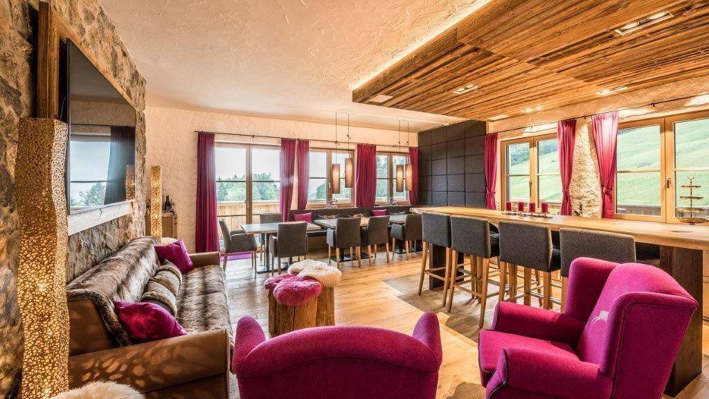 Offener Wohn- und Essbereich mit Holzbalkendecke, Steinwand und Blick auf die Landschaft.