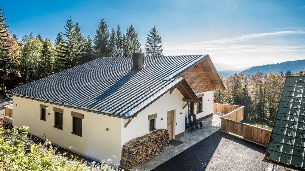 Charmantes Chalet mit Holzfassade, modernem Dach und gestapeltem Brennholz vor alpiner Kulisse.
