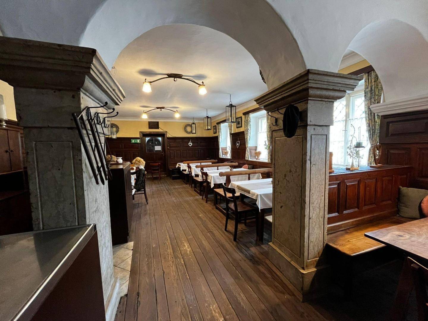 Langer Gastraum mit Holzböden, Holztischen, Bänken und einer beeindruckenden gewölbten Decke mit Säulen.