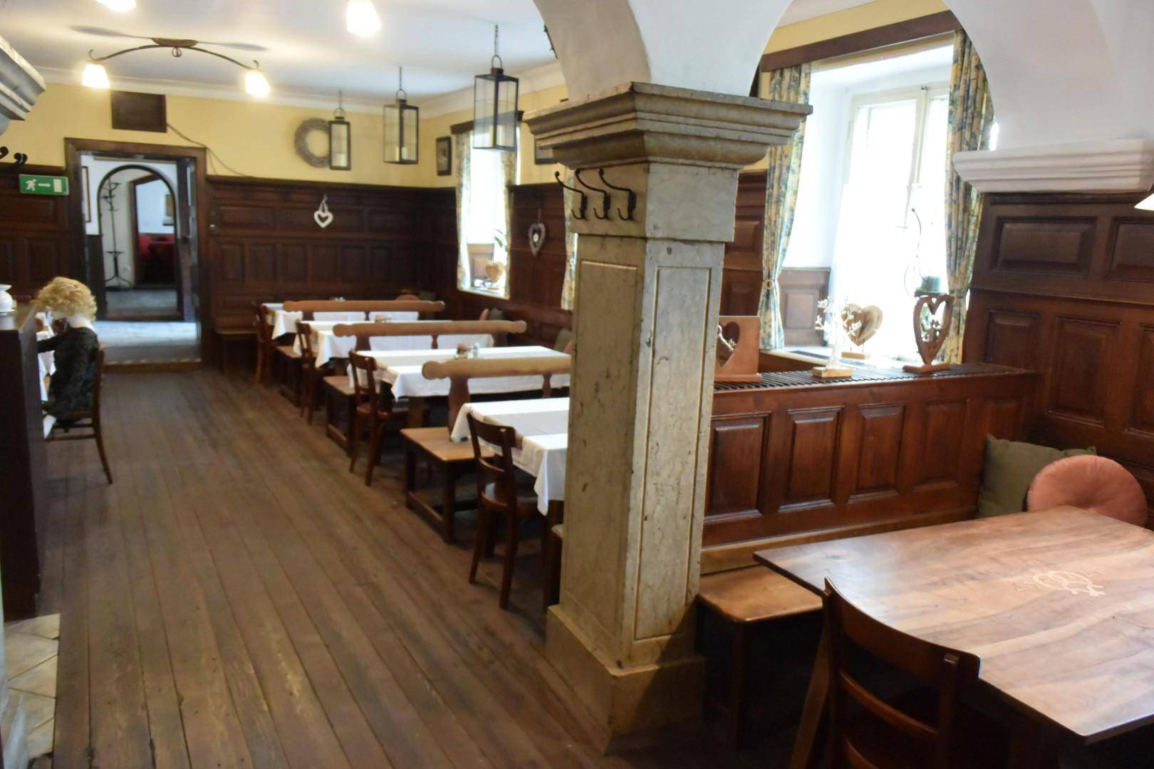 Gastraum mit Holzböden, Holzbänken, Tischen und einer steinernen Säule, die zur gewölbten Decke führt.
