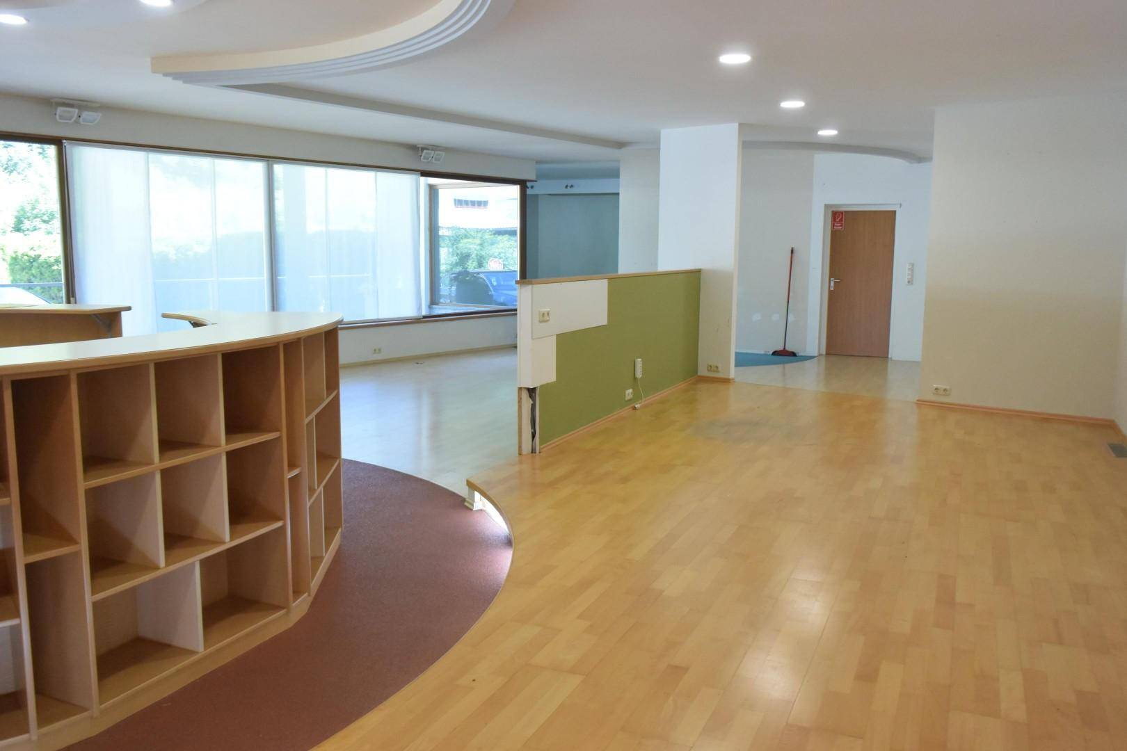Bürofläche mit geschwungenen Deckenstrukturen, Laminatboden und einer teilweisen grünen Wand, die den Raum gliedert.