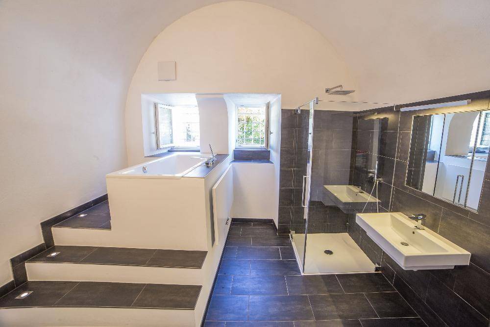 Modernes Badezimmer mit erhöhter Badewanne, begehbarer Dusche und dunklen Fliesen.