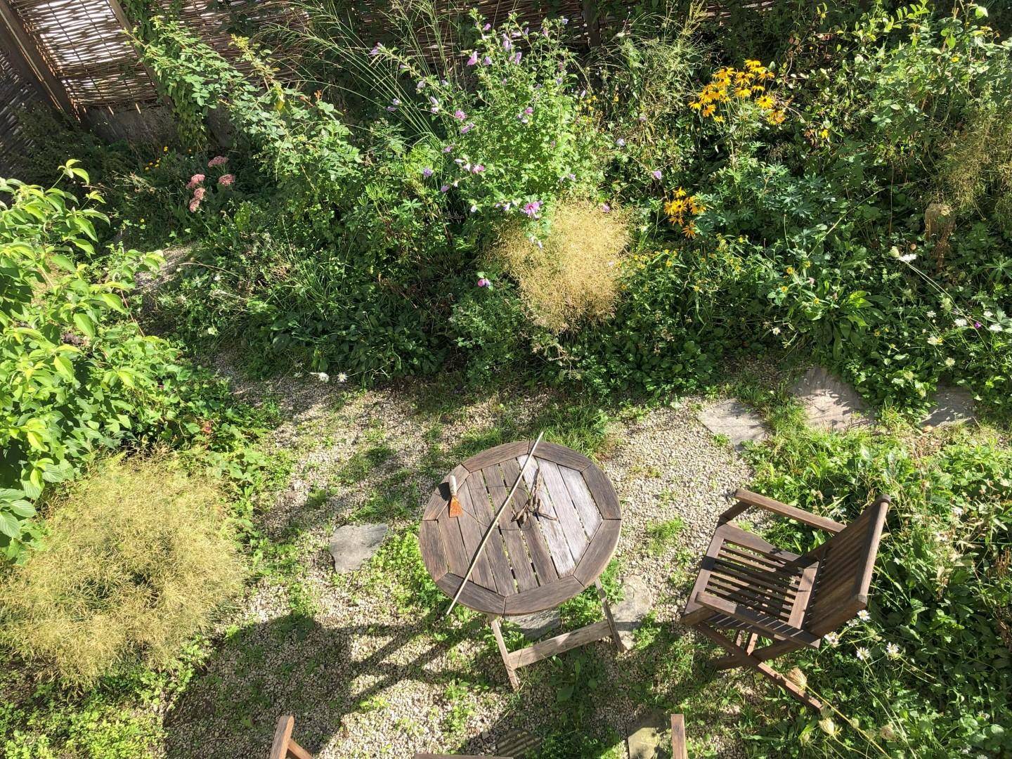 Blick von oben auf einen üppigen Garten mit Holztisch und Stühlen.