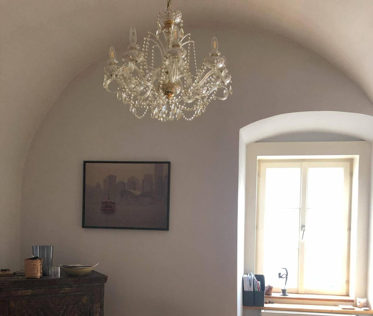 Raum mit gewölbter Decke, einem Fenster und einem eleganten Kronleuchter.