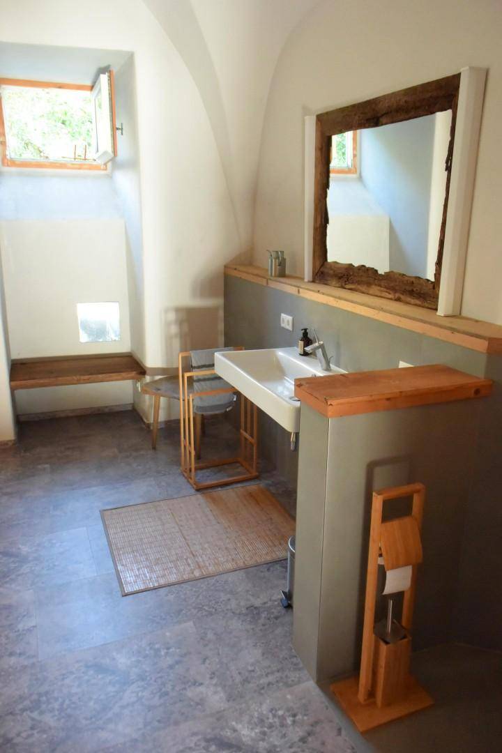 Badezimmer mit Einzelwaschbecken, Holzspiegelrahmen und Fenster für Tageslicht.