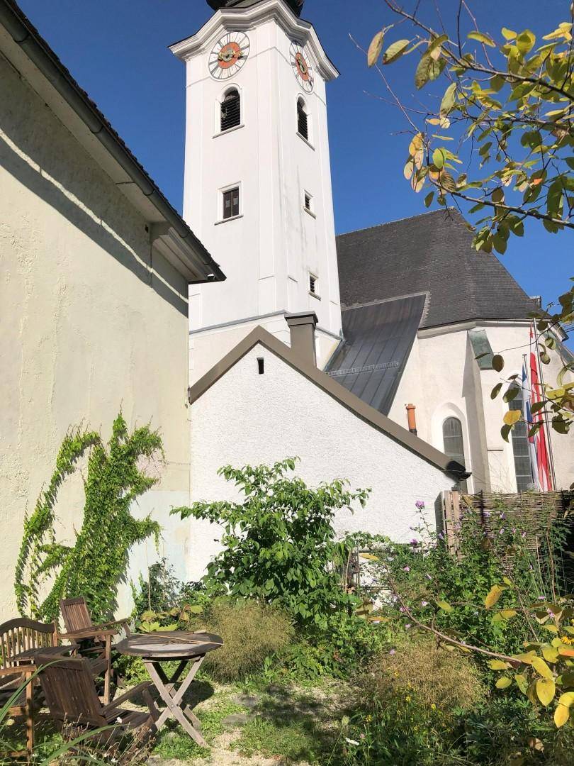 Gartenbereich mit Sitzgelegenheiten und Blick auf einen historischen Kirchturm.