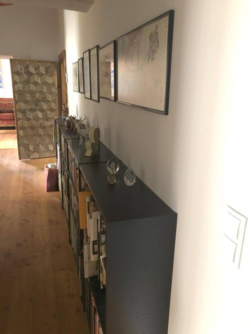 Langer Flur mit Bücherregal, gerahmten Bildern und Holzboden.