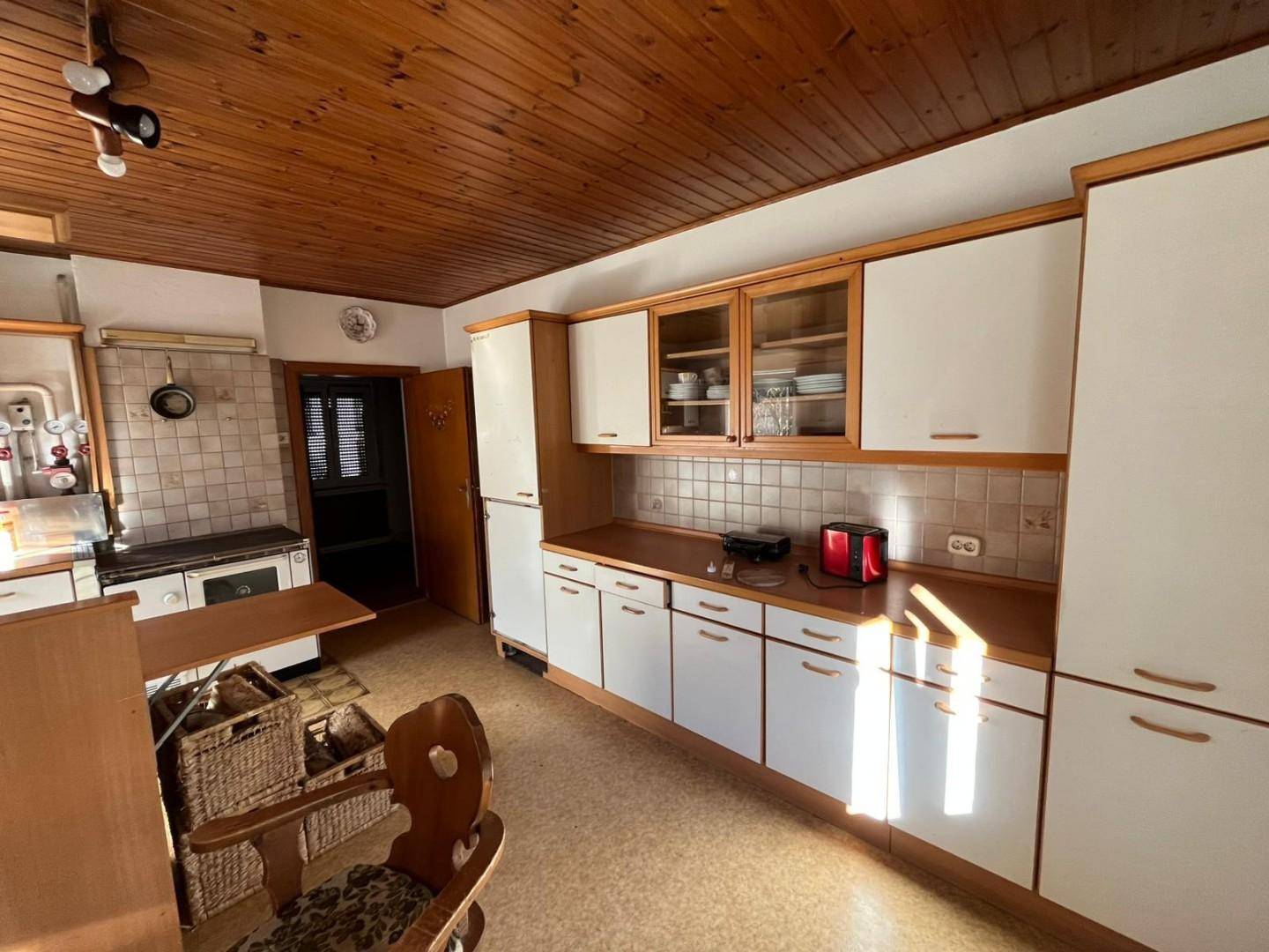 Traditionelle Küche mit Holzdecke, weißen Schränken und einem Holzofen, gut erhalten.