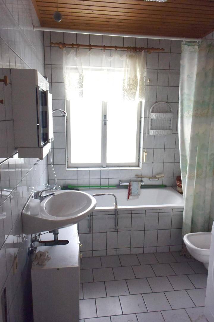 Helles Badezimmer mit Badewanne, Waschbecken und Fenster, komplett gefliest und sauber.