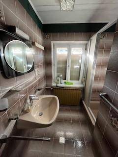 Modernisiertes Badezimmer mit Dusche, Waschbecken und Fenster, braun gefliest und gepflegt.
