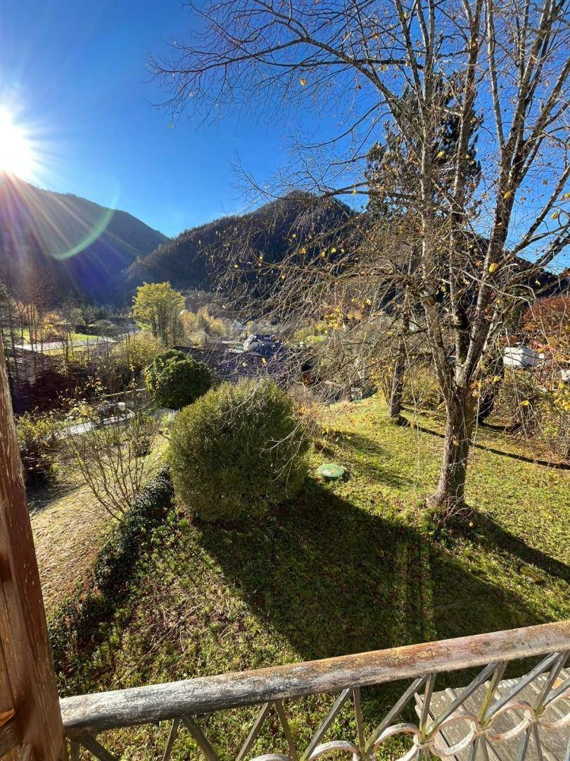 Balkon mit Blick auf den Garten und die malerische Berglandschaft unter blauem Himmel.