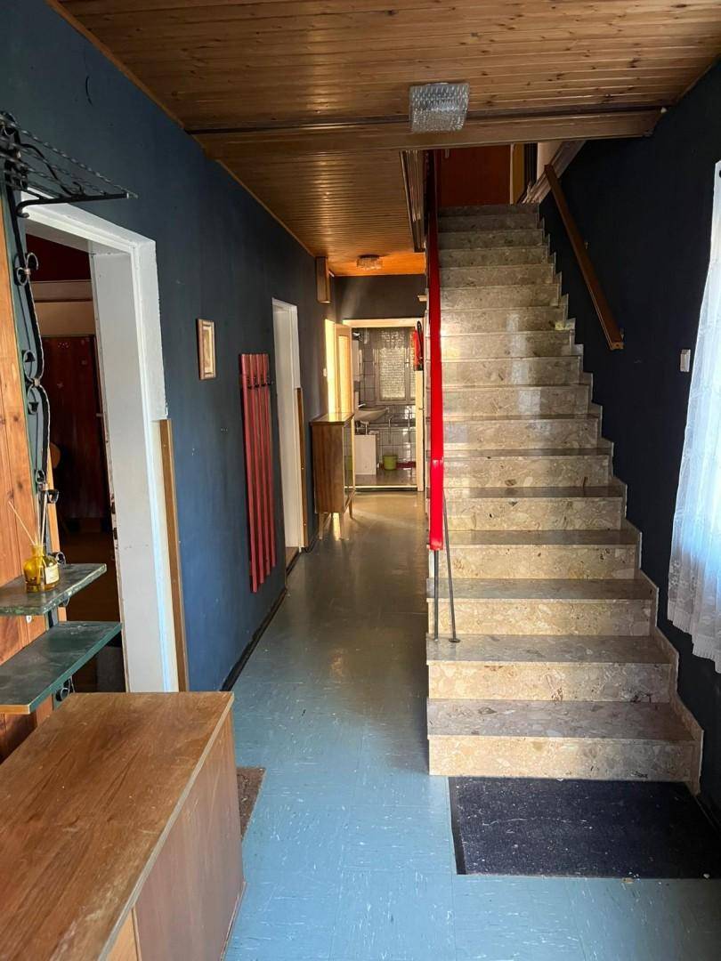 Flur mit Steintreppe, Holzdecke und dunklen Wänden, führt zu weiteren Räumen im Haus.