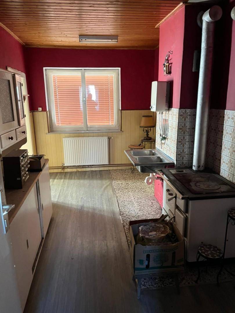 Rustikale Küche mit roten Wänden, Holzofen und Spülbecken unter dem Fenster, charmant und funktional.