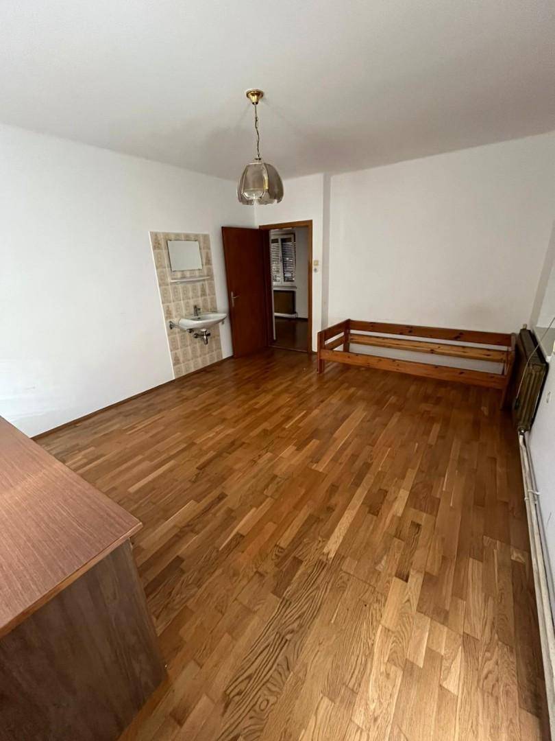 Geräumiges Schlafzimmer mit Holzdielenboden, Einzelbett und kleinem Waschbecken, hell und einfach.