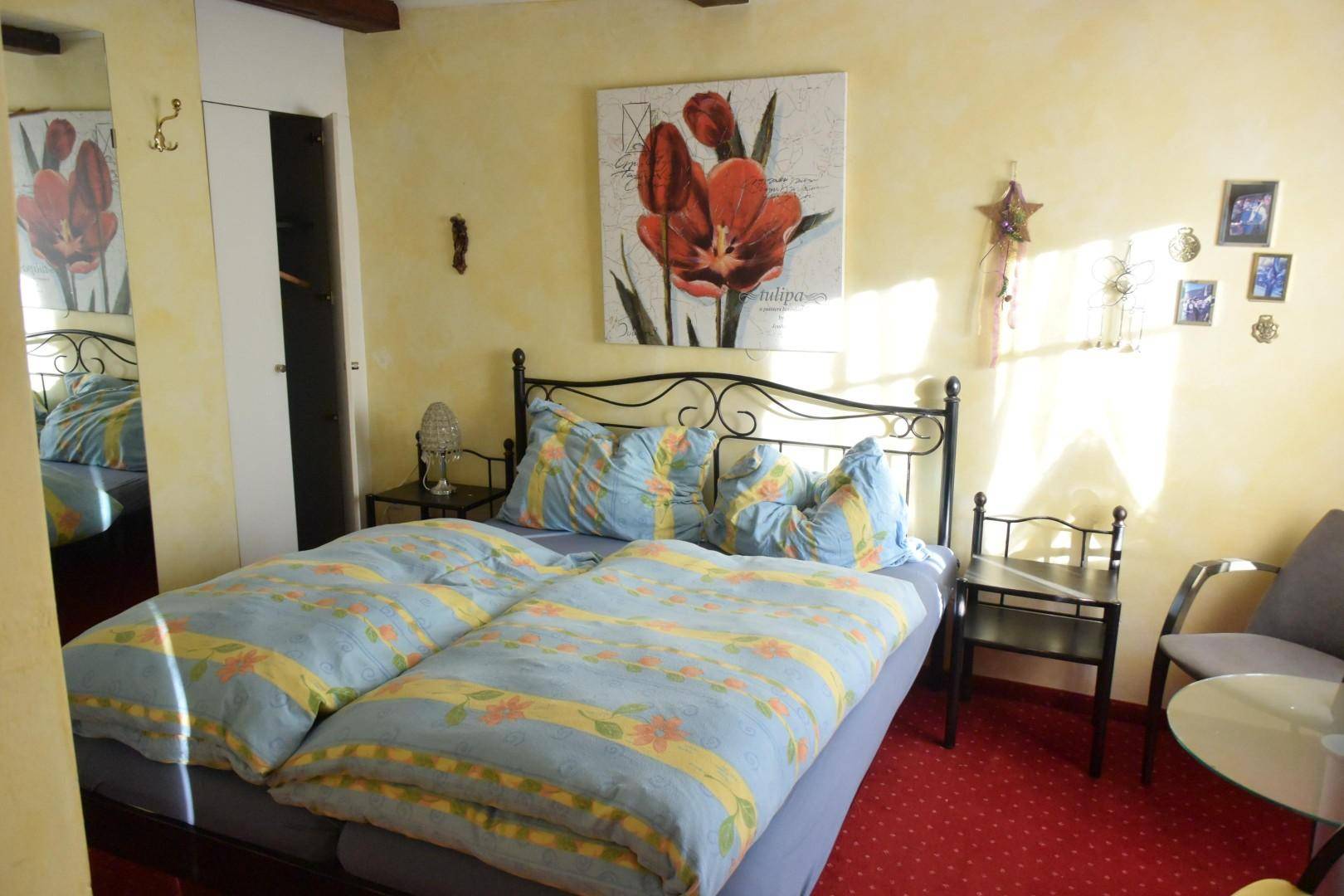 Gemütliches Schlafzimmer mit Doppelbett, rotem Teppichboden und gelben Wänden.