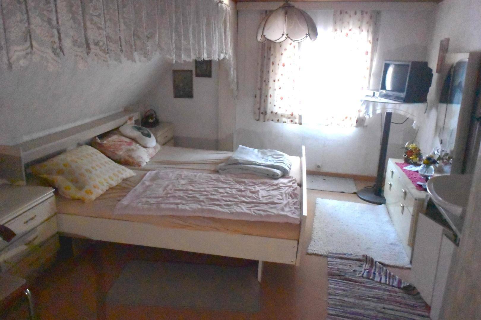 Dachschlafzimmer mit schrägen Wänden, Doppelbett und kleinem Waschbecken.