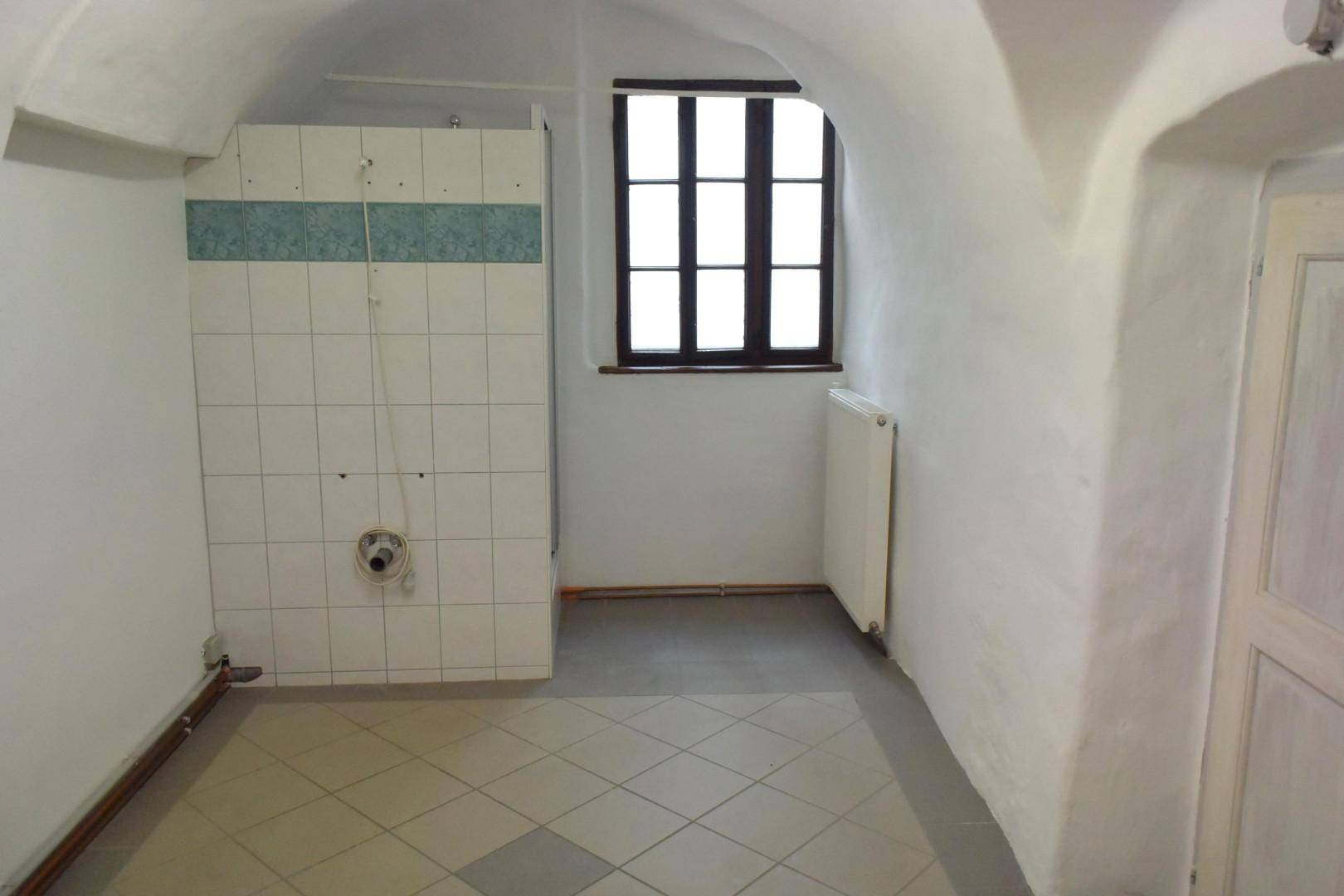 Badezimmer im Renovierungszustand mit Fliesenboden, einem Fenster und einer vorbereiteten Duschkabine unter einer Gewölbedecke.