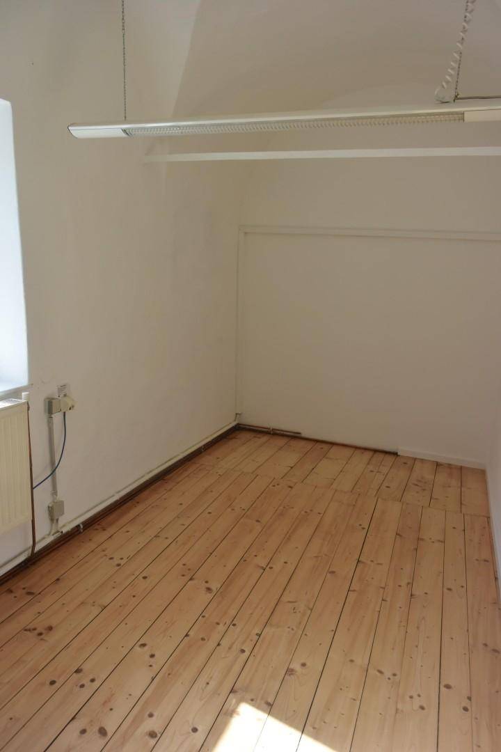 Schmaler Raum mit breiten Holzdielen, einem Fenster und einer einfachen Deckenleuchte, bereit für die individuelle Gestaltung.