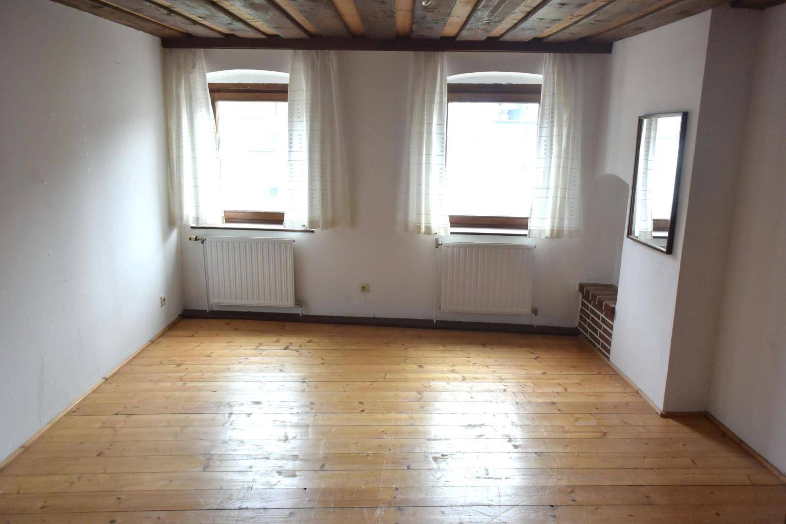 Geräumiges Zimmer mit Holzboden, zwei Fenstern und sichtbaren Deckenbalken.
