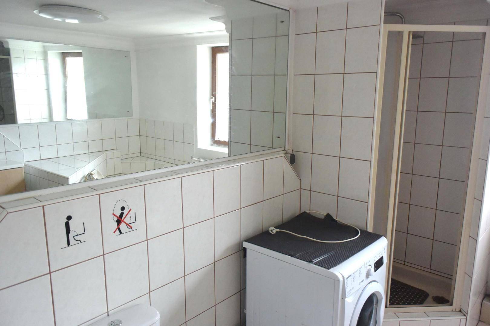 Badezimmer mit Duschkabine, weißen Fliesen und Platz für eine Waschmaschine.