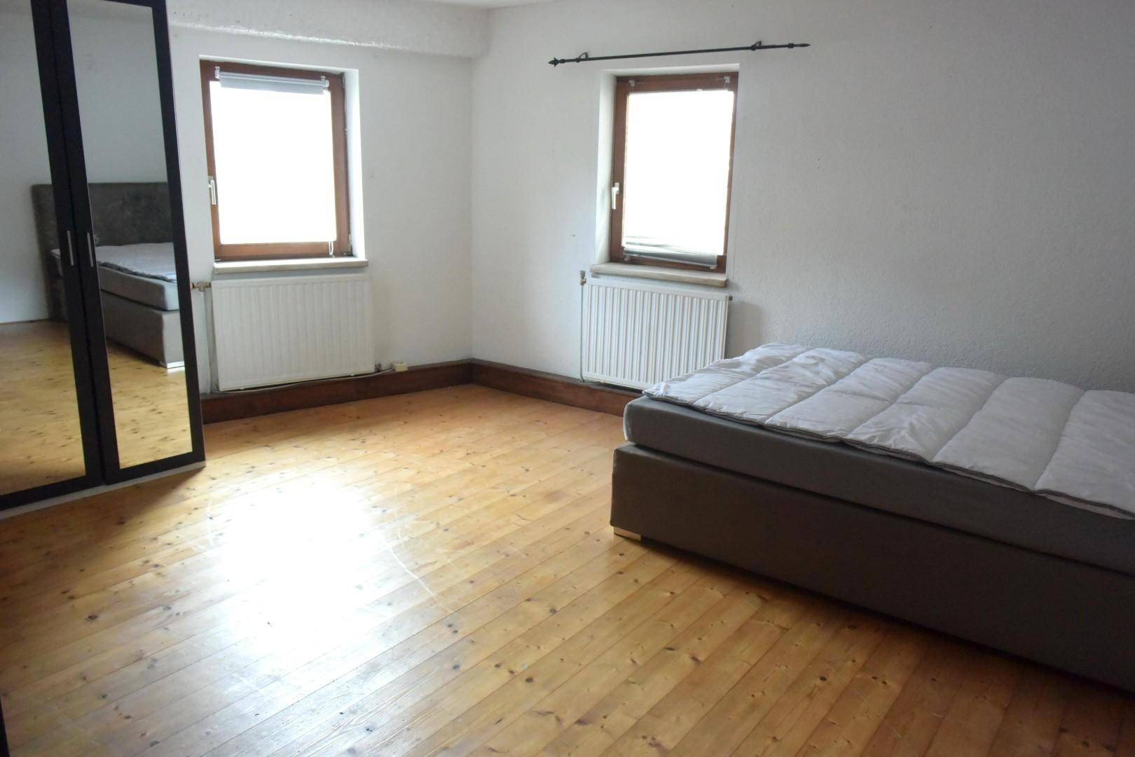 Helles Schlafzimmer mit Holzboden, Doppelbett und großem Spiegel an der Wand.