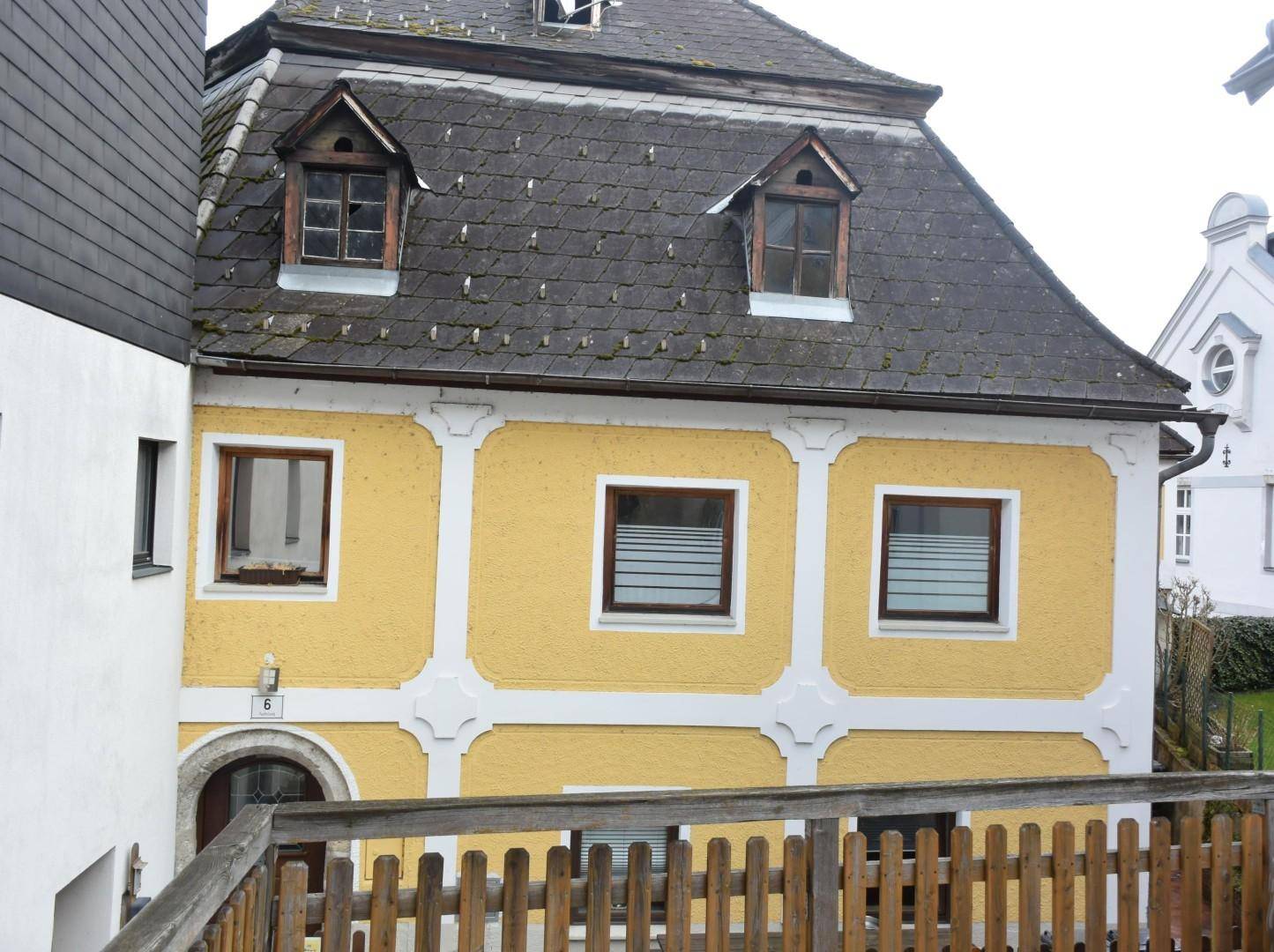Traditionelle Fassade mit gelbem Putz, weißen Zierelementen und einem Mansarddach mit Gaubenfenstern.